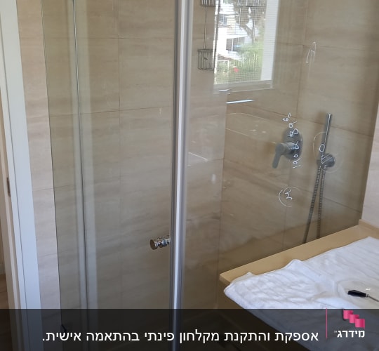 מקלחון זכוכית עם ברז ומגבת על השיש